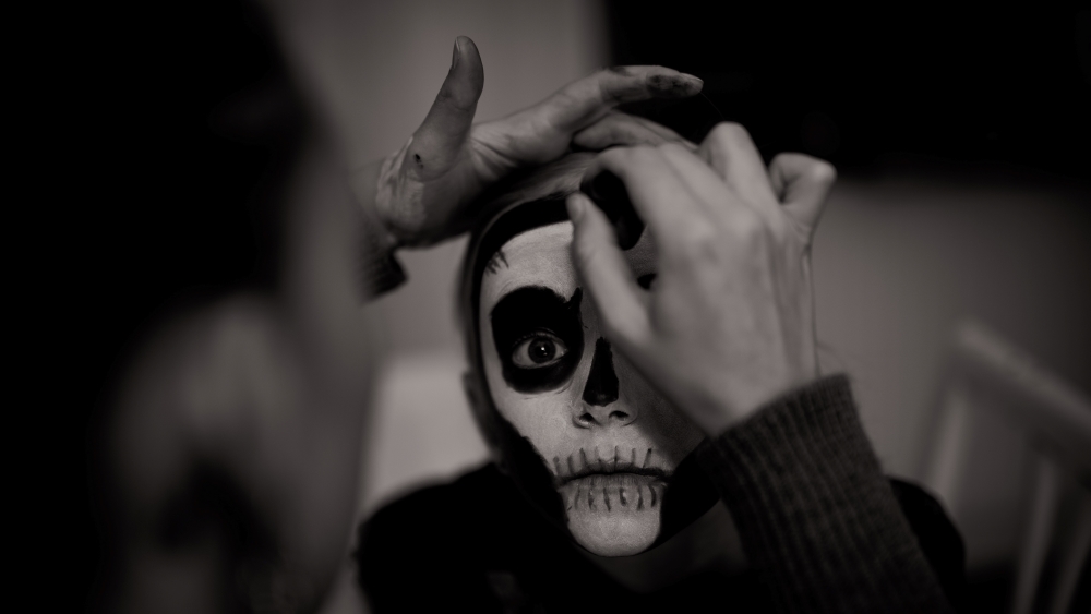 Black and white photo of a child having their face painted by an adult