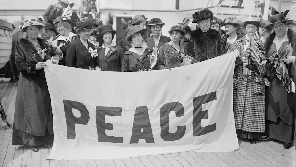 En gruppe med kvinner som holder et banner der det står "Peace"