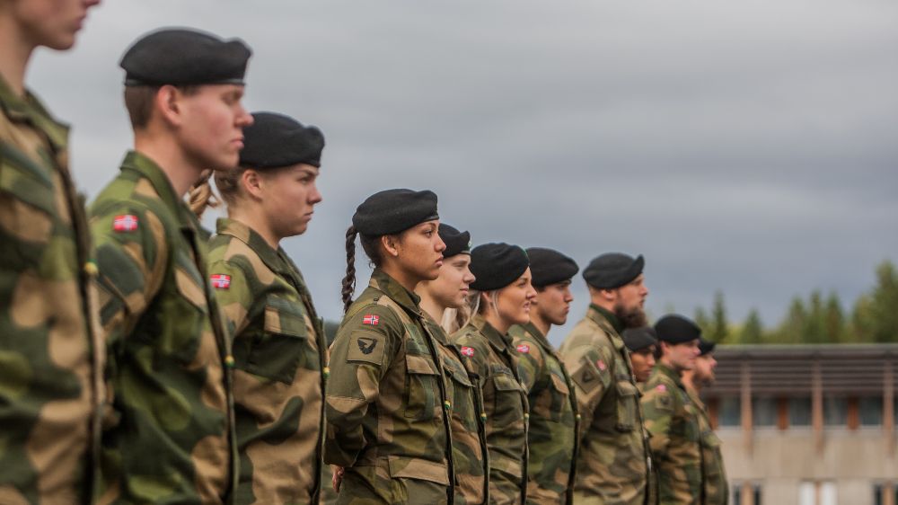 En rekke unge soldater i uniform står i profil