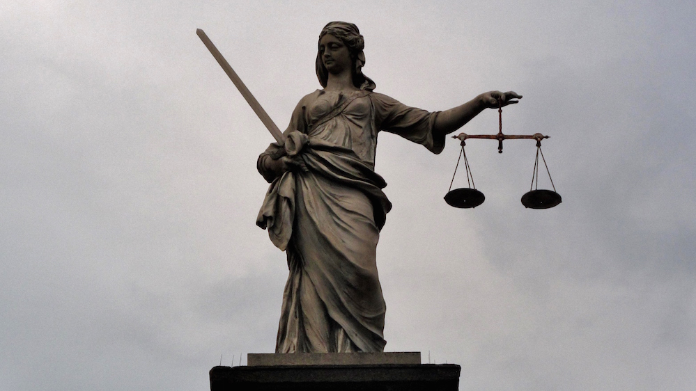 Bilde av statue av rettferdighetsgudinne mot mørk himmel